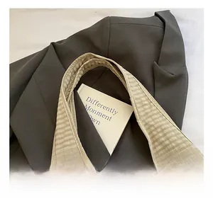 Detail view of khaki checkered canvas tote bag on a brown blazer with wide handle