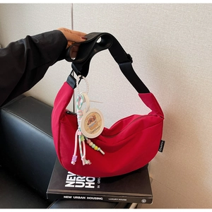 Detail view of red crescent nylon crossbody bag with cute Capybara charm and wide strap