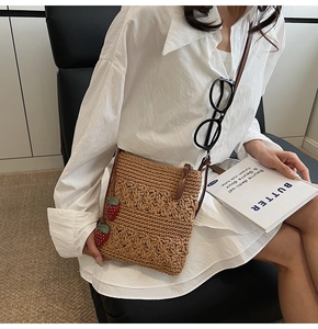 Detailed close-up of brown crochet straw crossbody bag with strawberry pendants and leather strap