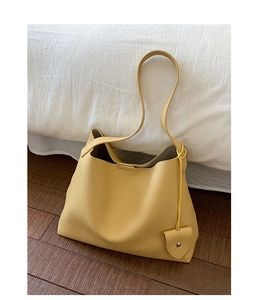 Dettaglio borsa tote gialla in pelle con trama litchi e ciondolo a cuore su pavimento