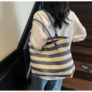 Vue de dos d'un mannequin portant le grand sac cabas tissé à rayures bleues et beige sur un escalier