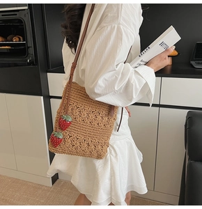 Detail of hand-woven brown crochet bag featuring 3D red strawberry charms and leather strap