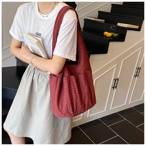 Detail of red checkered tote bag showing functional side pockets and wide canvas shoulder strap