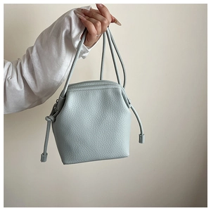 Detailed close-up of light blue pebbled leather crossbody bag with minimalist knot handle