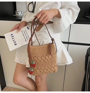 Close-up of woven shoulder bag with strawberry charms and brown synthetic leather straps