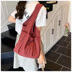 Detail of red checkered canvas tote bag with side pocket shown on a shoulder