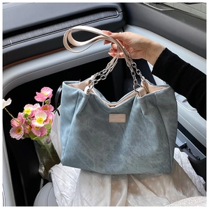 Detail of light blue corduroy tote bag with chain strap and vintage leather patch label