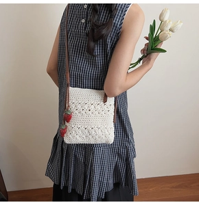 Close-up of white crochet crossbody bag with red strawberry charms and slim brown strap