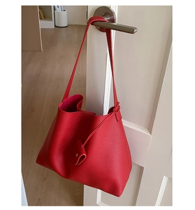 Dettaglio della borsa tote in pelle rossa con trama a litchi appesa a una porta bianca