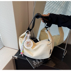 Detail of cream nylon crescent bag with wide black strap and cute capybara charm accessory