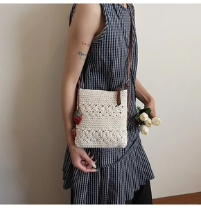 Detail of hand-woven cream crossbody bag with strawberry charms and brown strap
