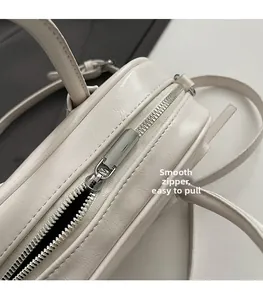 Détail d'un sac Boston en PU crème avec une fermeture éclair argentée fluide et texture cuir