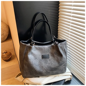 Detailed macro shot of the gray canvas tote bag featuring black leather handles and text logo