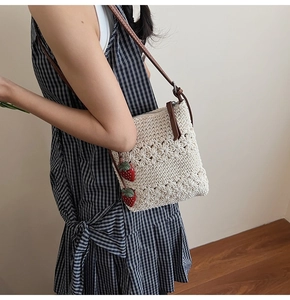 Detail of crochet square bag with floral texture, brown strap and strawberry charms