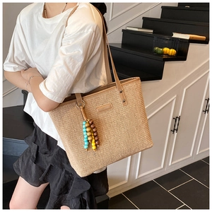 Detail of straw tote bag featuring colorful wooden bead tassel and leather strap