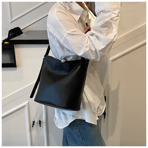 Détail d'un sac seau en cuir noir avec fermoir sphérique argenté porté par un mannequin