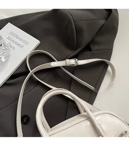 Détail du sac à main en cuir verni blanc avec boucle argentée sur tissu marron foncé