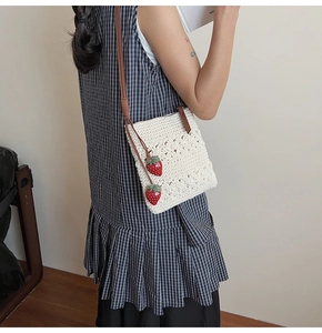 Detail of cream crochet knit bag featuring brown leather strap and strawberry charms