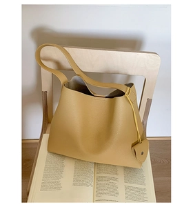 Dettaglio della borsa tote in pelle giallo senape con ciondolo a cuore su sedia in legno