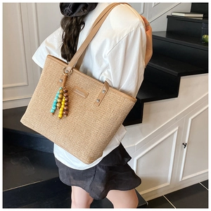 Detail of bohemian straw tote with colorful wooden beads tassel and brown leather strap