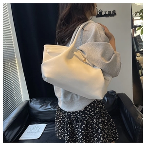 Detail of white leather tote bag with drawstring pleats and gold hardware on a model