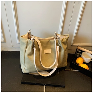 Detail of light green canvas tote bag with leather straps on a black book and tray