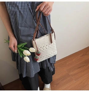 Detail of white crochet square bag with red strawberry charms and brown leather strap