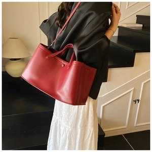 Fashionable red leather tote bag with round gold buckle detail on an indoor staircase