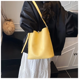 Détail du sac seau jaune en cuir grainé avec fermoir à bille argentée porté par un mannequin