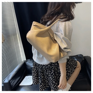 Detailed view of beige leather tote bag with soft texture and slim handles on model