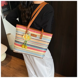 Detail of a colorful striped straw beach bag with leather handles and a flower charm