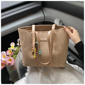 Detail of hand-woven straw tote bag with brown leather strap and colorful wooden beads