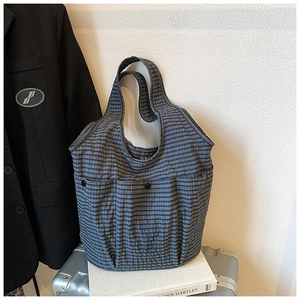Close-up of grey plaid canvas tote bag featuring dual front pockets with black button closures
