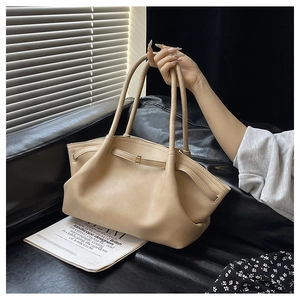 Close-up of beige leather tote bag with metal buckle on a black leather sofa