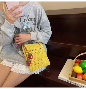 Detail shot of yellow hand-crocheted bag with red strawberry charms and floral texture