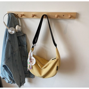 Detail of yellow canvas hobo bag with black strap and colorful cartoon charm on wood hook