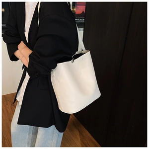 Gros plan d'un sac seau blanc à motif litchi avec boucle argentée porté par un mannequin