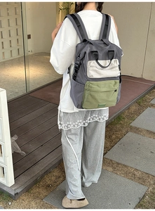 Detail view of a grey canvas backpack with green and white color-block zipper pockets