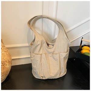 Detail view of a beige checkered tote bag featuring two front button pockets in a home setting