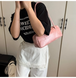 Detailed view of pink leather baguette bag worn as a shoulder bag on minimalist model