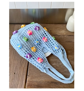 Detail of light blue crochet tote bag with colorful 3D floral accents and open knit texture