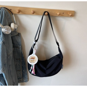 Detail of black nylon dumpling bag with adjustable strap and capybara charm