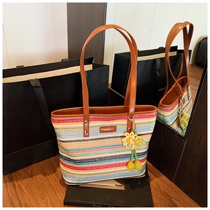 Detail of multi-color woven straw tote bag with brown leather handles and sunflower charm