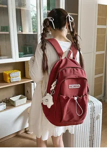 Detail of burgundy nylon backpack with RKDBAG embroidery and white plush bear charm