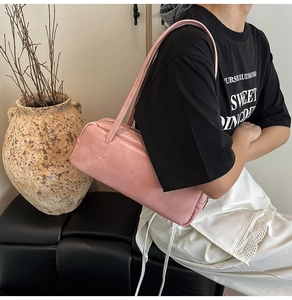 Minimalist light pink leather Boston bag worn on shoulder by a model in a lifestyle setting
