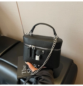 Detail of black litchi grain leather texture and silver chain strap on crossbody bag