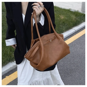 Close-up of brown leather tote bag with side fold structure and metal buckle detail