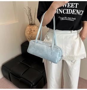 Detail view of a light blue baguette bag with dual straps and smooth faux leather texture