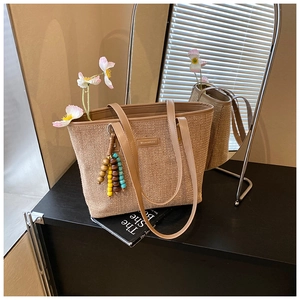 Detailed texture of beige straw tote bag with brown leather handles and bead charm
