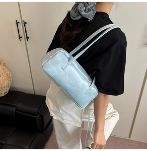 Light blue glossy leather rectangular underarm bag worn by a model in a casual setting